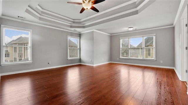 empty room featuring dark wood-type flooring, a tray ceiling, a healthy amount of sunlight, and visible vents