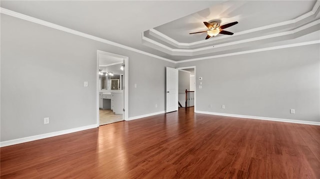 spare room featuring a tray ceiling, crown molding, baseboards, and wood finished floors