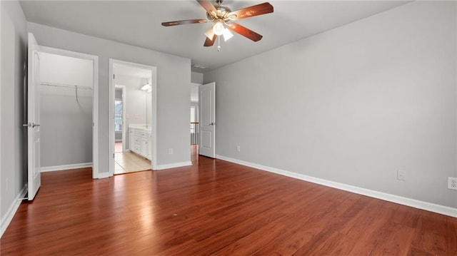 unfurnished bedroom featuring a closet, a spacious closet, ensuite bathroom, wood finished floors, and baseboards