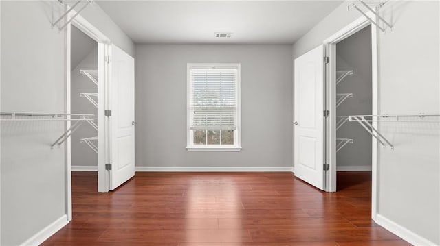 unfurnished bedroom with a closet, visible vents, a spacious closet, wood finished floors, and baseboards