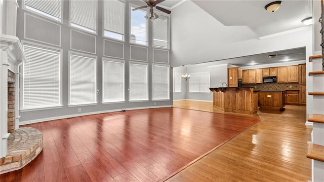 living room with a high ceiling, ornamental molding, light wood-style floors, baseboards, and ceiling fan with notable chandelier