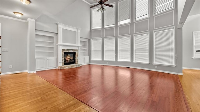 unfurnished living room with wood finished floors, a glass covered fireplace, a ceiling fan, and baseboards