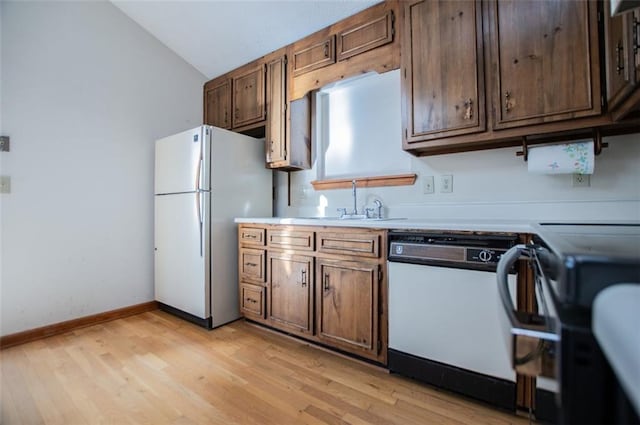 kitchen with light wood-type flooring, white appliances, vaulted ceiling, and sink