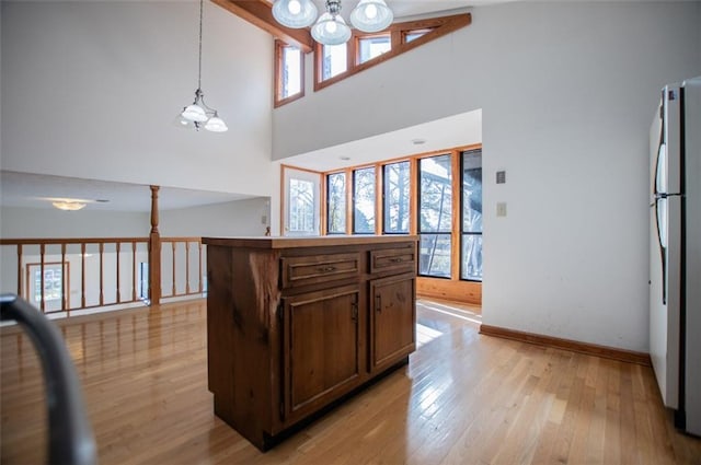 kitchen featuring a center island, stainless steel fridge, a towering ceiling, a chandelier, and light wood-type flooring