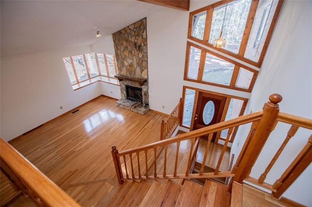 staircase featuring wood-type flooring, high vaulted ceiling, a wealth of natural light, and a stone fireplace