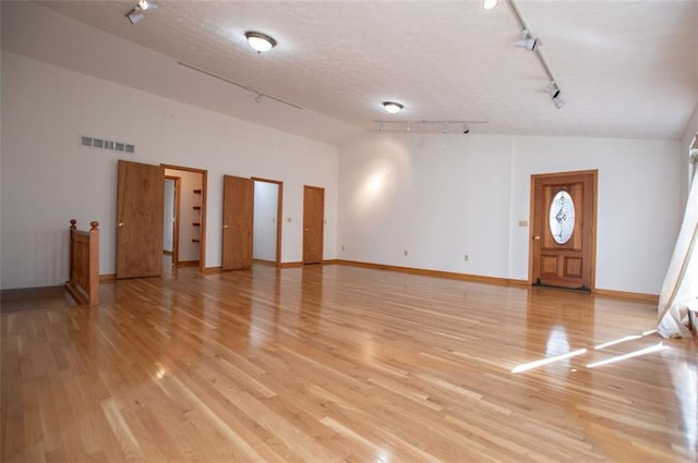 unfurnished living room featuring a textured ceiling, light hardwood / wood-style floors, rail lighting, and high vaulted ceiling