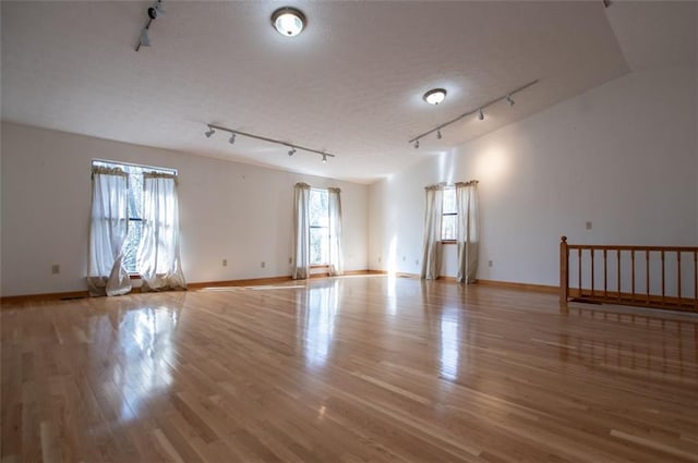 empty room with a textured ceiling, light wood-type flooring, and track lighting