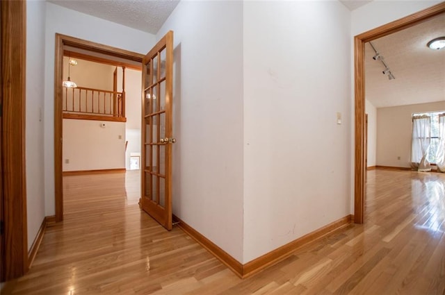 hallway with rail lighting, a textured ceiling, and light wood-type flooring