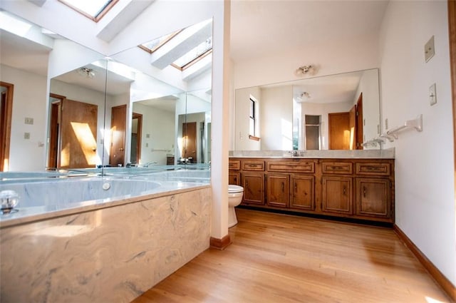 bathroom featuring vanity, hardwood / wood-style flooring, toilet, and vaulted ceiling with skylight