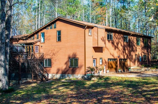 back of property featuring a lawn, a garage, and a deck