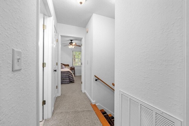 hall featuring a textured ceiling and light colored carpet