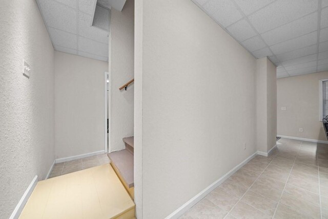 corridor with a drop ceiling and light tile patterned floors