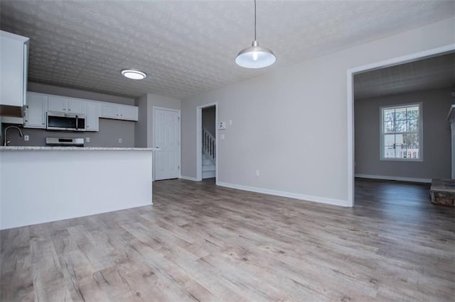 kitchen with light wood-type flooring, stainless steel microwave, open floor plan, white cabinets, and light countertops