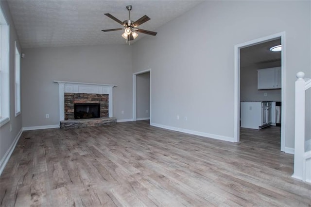 unfurnished living room with baseboards, ceiling fan, lofted ceiling, a fireplace, and wood finished floors