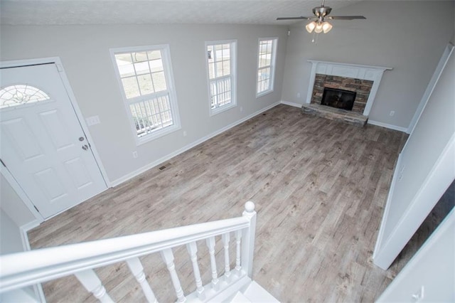 foyer featuring a stone fireplace, baseboards, ceiling fan, and wood finished floors