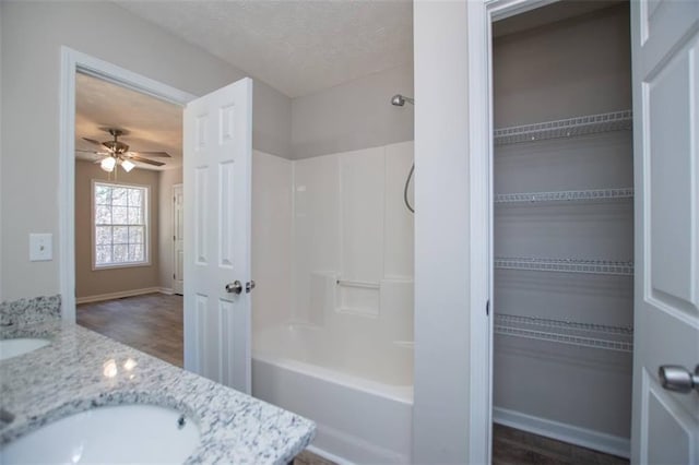 bathroom featuring ceiling fan, double vanity, shower / bathtub combination, a textured ceiling, and a sink