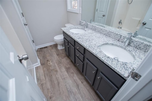 bathroom with a sink, toilet, wood finished floors, and double vanity