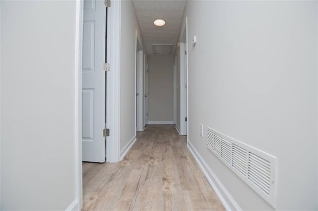 hallway with light wood finished floors, visible vents, and baseboards