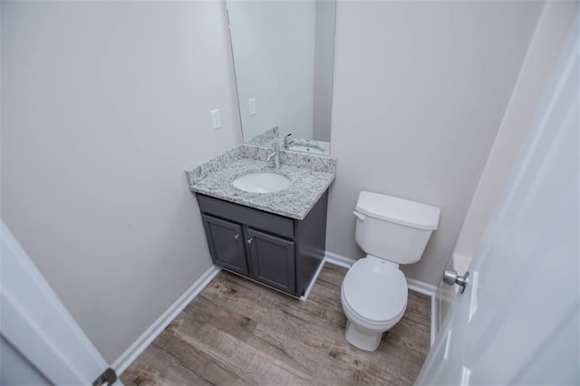 bathroom featuring baseboards, toilet, wood finished floors, and vanity