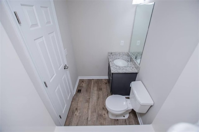 half bath featuring vanity, wood finished floors, visible vents, baseboards, and toilet