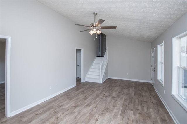 unfurnished living room with wood finished floors, baseboards, lofted ceiling, ceiling fan, and a textured ceiling