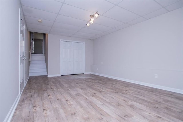 unfurnished bedroom featuring wood finished floors, a paneled ceiling, a closet, and baseboards