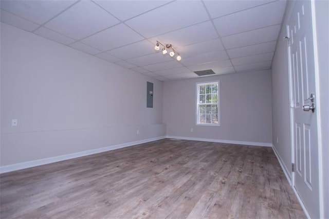 spare room featuring electric panel, baseboards, a paneled ceiling, and wood finished floors