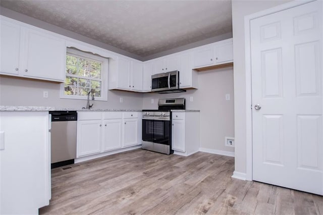 kitchen featuring light wood-style flooring, a sink, appliances with stainless steel finishes, white cabinets, and baseboards