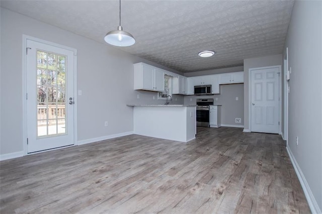 kitchen with a peninsula, white cabinets, plenty of natural light, and appliances with stainless steel finishes