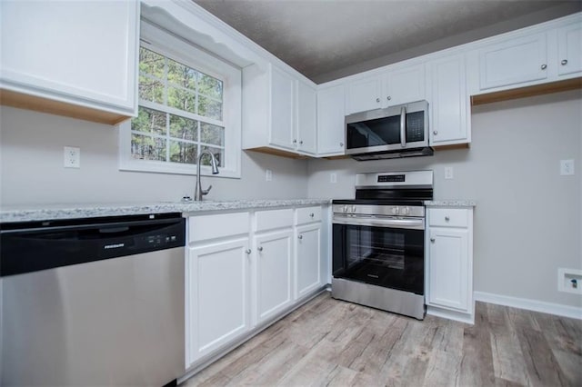 kitchen featuring a sink, light wood-style floors, appliances with stainless steel finishes, white cabinets, and baseboards