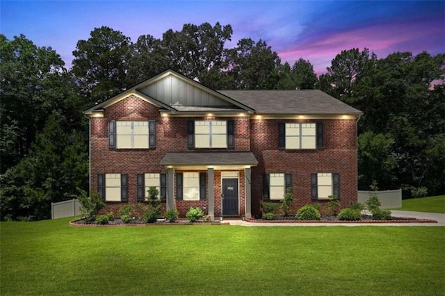 view of front of property featuring fence, a lawn, and brick siding