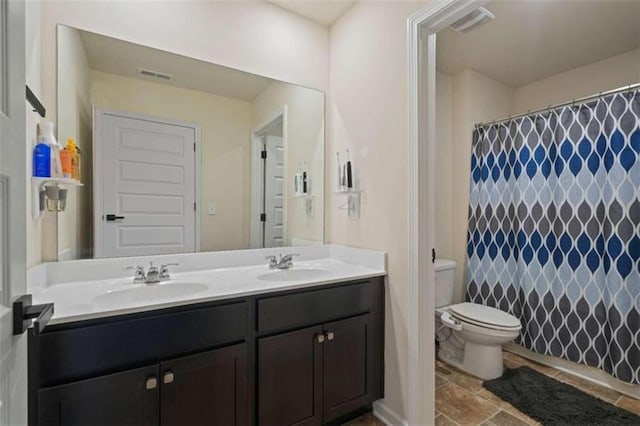 bathroom with visible vents, double vanity, a sink, and toilet