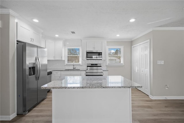 kitchen with crown molding, white cabinets, light wood finished floors, and appliances with stainless steel finishes