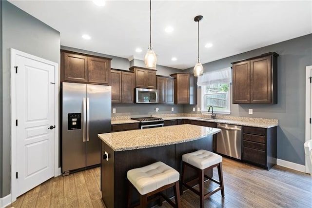 kitchen featuring pendant lighting, stainless steel appliances, a kitchen bar, a kitchen island, and sink