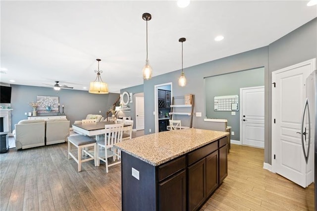 kitchen with light hardwood / wood-style floors, hanging light fixtures, ceiling fan, a kitchen island, and dark brown cabinetry