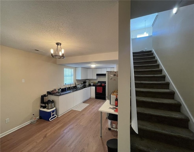 kitchen featuring black gas range oven, white cabinetry, light wood finished floors, dark countertops, and baseboards
