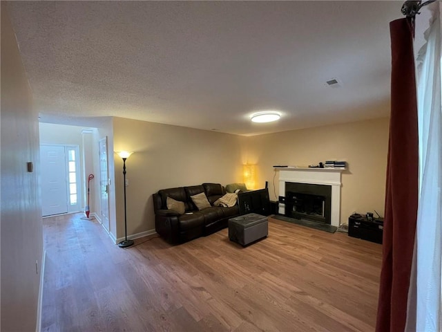 living area with wood finished floors, a fireplace with raised hearth, baseboards, and a textured ceiling