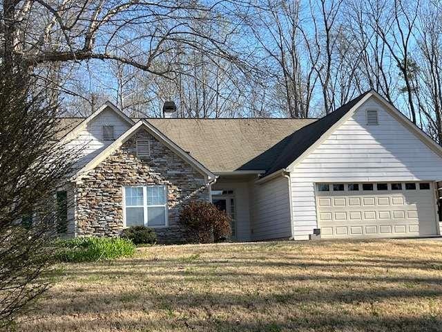 single story home featuring stone siding, a front yard, a garage, and a chimney