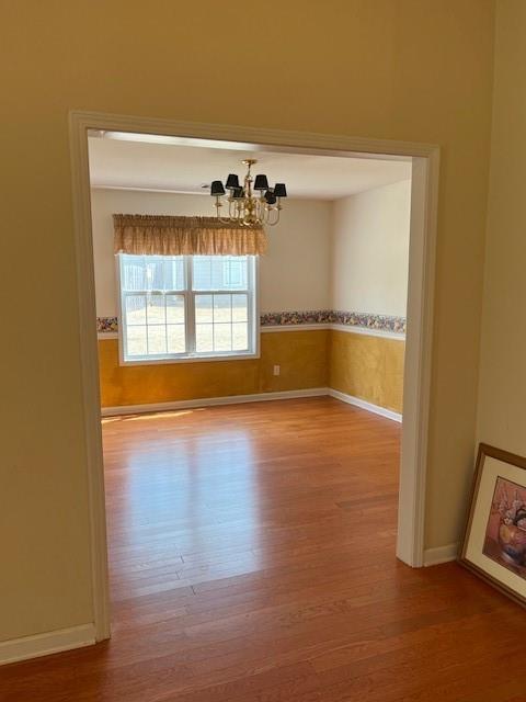 unfurnished room featuring baseboards, a chandelier, and wood finished floors