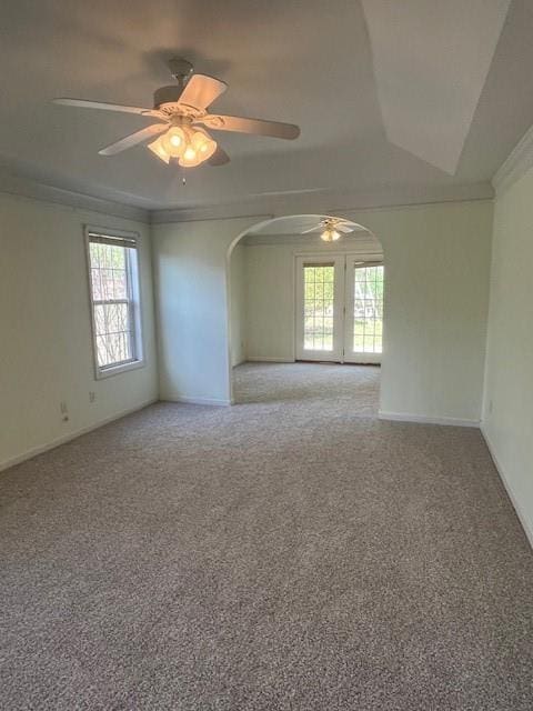 spare room with crown molding, carpet floors, baseboards, arched walkways, and ceiling fan