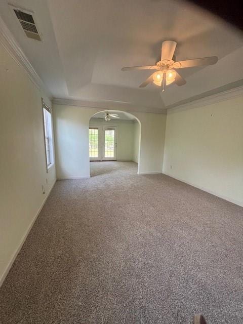 carpeted spare room featuring crown molding, a raised ceiling, arched walkways, ceiling fan, and visible vents