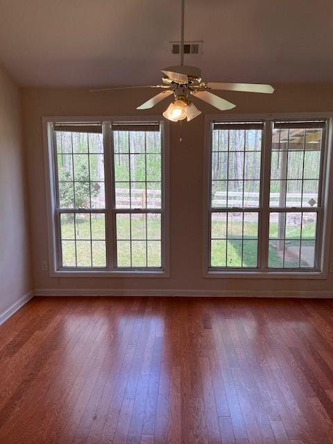 empty room with baseboards, visible vents, ceiling fan, and hardwood / wood-style flooring