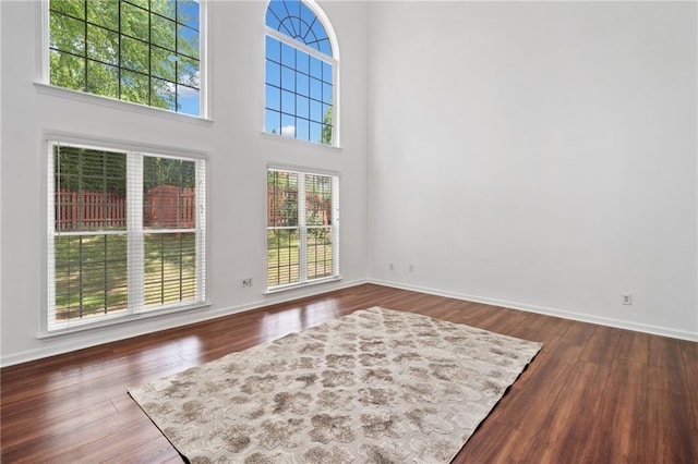 unfurnished living room with baseboards, wood finished floors, and a high ceiling