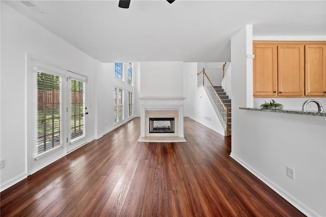 unfurnished living room with a ceiling fan, dark wood finished floors, stairs, a multi sided fireplace, and a sink