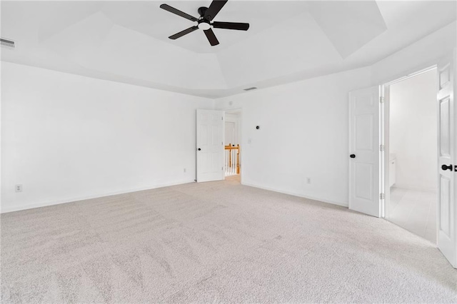 spare room featuring a tray ceiling, light colored carpet, and a ceiling fan