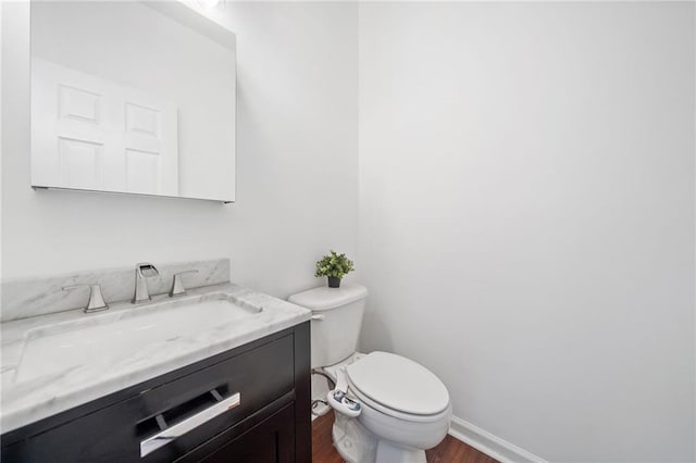 bathroom with toilet, baseboards, vanity, and wood finished floors