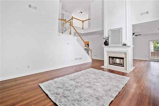 living room featuring a glass covered fireplace, stairs, a towering ceiling, wood finished floors, and ceiling fan
