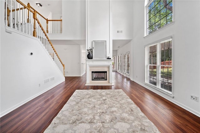 living area featuring healthy amount of natural light, a towering ceiling, dark wood finished floors, and baseboards