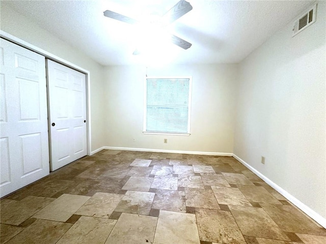 unfurnished bedroom with a closet, visible vents, stone finish flooring, ceiling fan, and baseboards