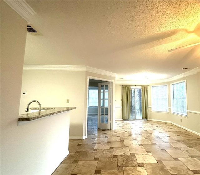 spare room featuring baseboards, visible vents, a textured ceiling, crown molding, and a sink